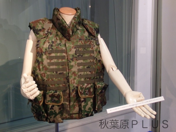 防弾チョッキ2型。装具取り付け用のウェビングが多く縫い付けられている。通常であれば戦闘服と同じ迷彩がほどこされるが、本作では、3型とは柄の違う「迷彩服4型」に合わせ近いOD色となっている。
